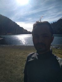 Portrait of man standing by lake against sky