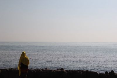 Rear view of man standing in sea against clear sky