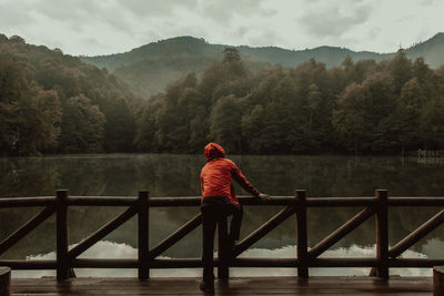 Man standing on railing by lake against mountains