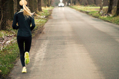 Rear view of woman jogging on road amidst trees