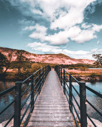 Footbridge leading towards mountains against sky