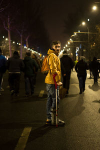 Disabled man standing against people walking on road during protest at night