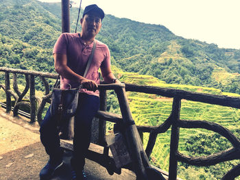 Young man standing on railing against trees