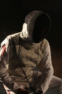 Man holding sword while sitting in darkroom at night