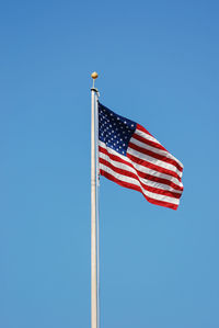 Low angle view of flag against clear blue sky