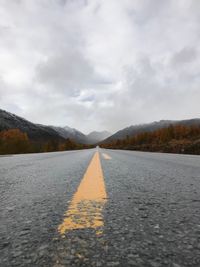 Surface level shot of road leading towards mountain against cloudy sky