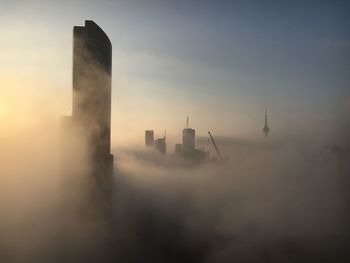 Buildings and cranes in city against sky during foggy weather