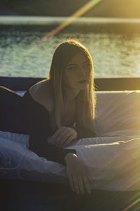 Young woman lies putting his hand downon a mattress on the water and the sunset illuminates her hair