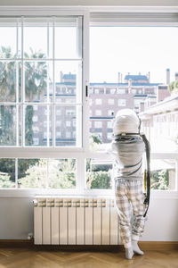 Back view of child wearing pajama and looking through a window with an astronaut helmet