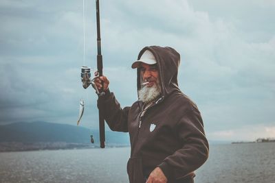 Man holding umbrella by sea against sky