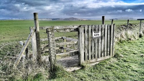 Fence on field against cloudy sky