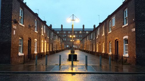 Illuminated street light amidst buildings against sky at dusk