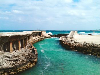 Scenic view of old ruins at sea against cloudy sky