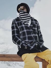 Low angle view of man sitting on railing outside snow against sky