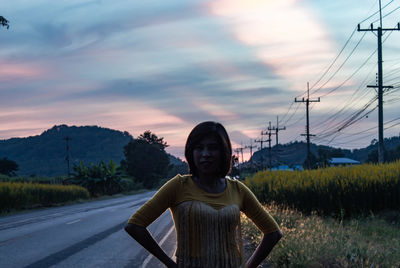 Portrait of man standing on road against sky during sunset