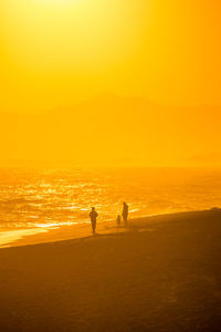 Silhouette people standing on beach against sky during sunset