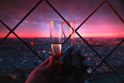 Midsection of person holding drink against sky during sunset