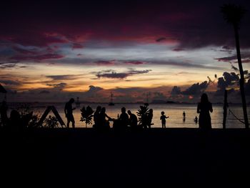 Silhouette people on beach against sky during sunset