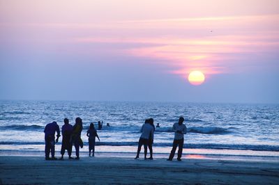 Silhouette people standing on beach against sky during sunset