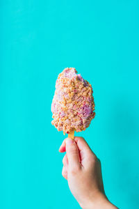 Cropped hand of person holding ice cream against blue background
