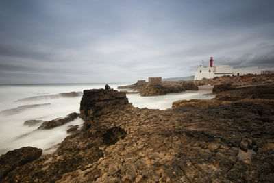 Lighthouse on cliff by sea against sky