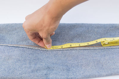 Close-up of person taking measurement of jeans over white background