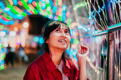 Smiling young woman looking at illuminated multi colored lighting equipment 