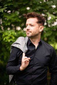 Young man looking away while standing against plants