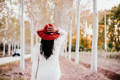 Woman wearing hat standing against trees