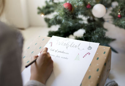 Cropped image of girl writing on paper by christmas tree at home