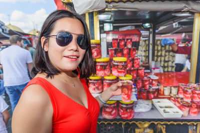 Portrait of woman wearing sunglasses holding food while standing in market