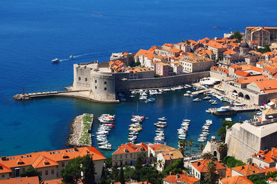 High angle view of cityscape by sea against blue sky