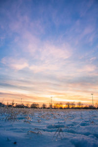 Snow covered land against sky during sunset