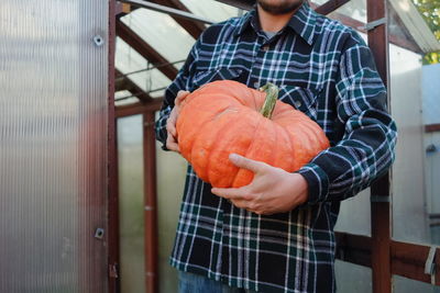 Midsection of man holding pumpkin while standing outdoors