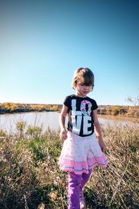 Girl looking down while walking on field against sky