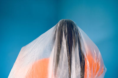 Teenage girl wrapped in plastic against blue background