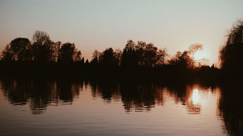 Silhouette trees by lake against sky during sunset