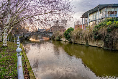 Bridge over river by buildings against sky
