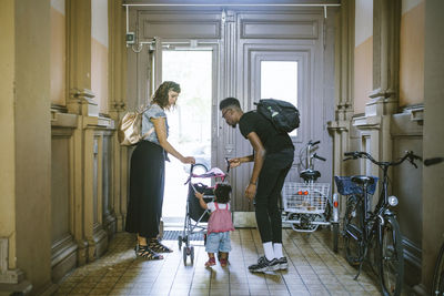 Mother and father looking at daughter pushing baby stroller in corridor of apartment