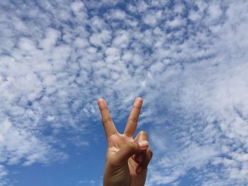 Cropped hand gesturing peace sign against blue sky