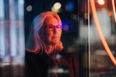 Wrinkled woman looking away while standing in city at night