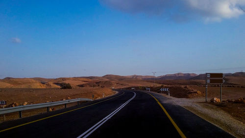 Empty road along landscape against blue sky