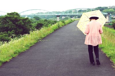 Full length rear view of woman with umbrella walking on street against bridge