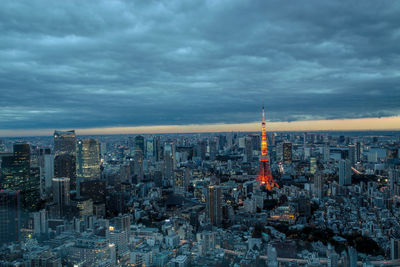 Aerial view of illuminated tokyo tower amidst buildings against cloudy sky