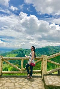 Side view of woman standing on mountain against cloudy sky