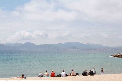 People relaxing on beach against sky