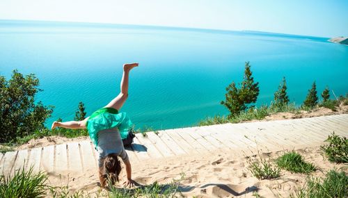 Rear view of girl practicing cartwheel at shore of lake michigan