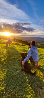 Rear view of woman sitting on field against sky during sunset