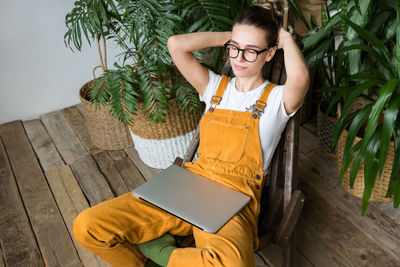 Woman with laptop napping while sitting on chair at home