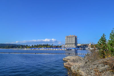 Scenic view of sea by buildings against clear blue sky